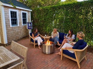 Un patio con mobiliario exterior, una chimenea y un pequeño edificio con ventanas.