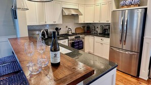 A modern kitchen with white cabinets, stainless steel appliances, and a wooden island with wine glasses and a bottle.