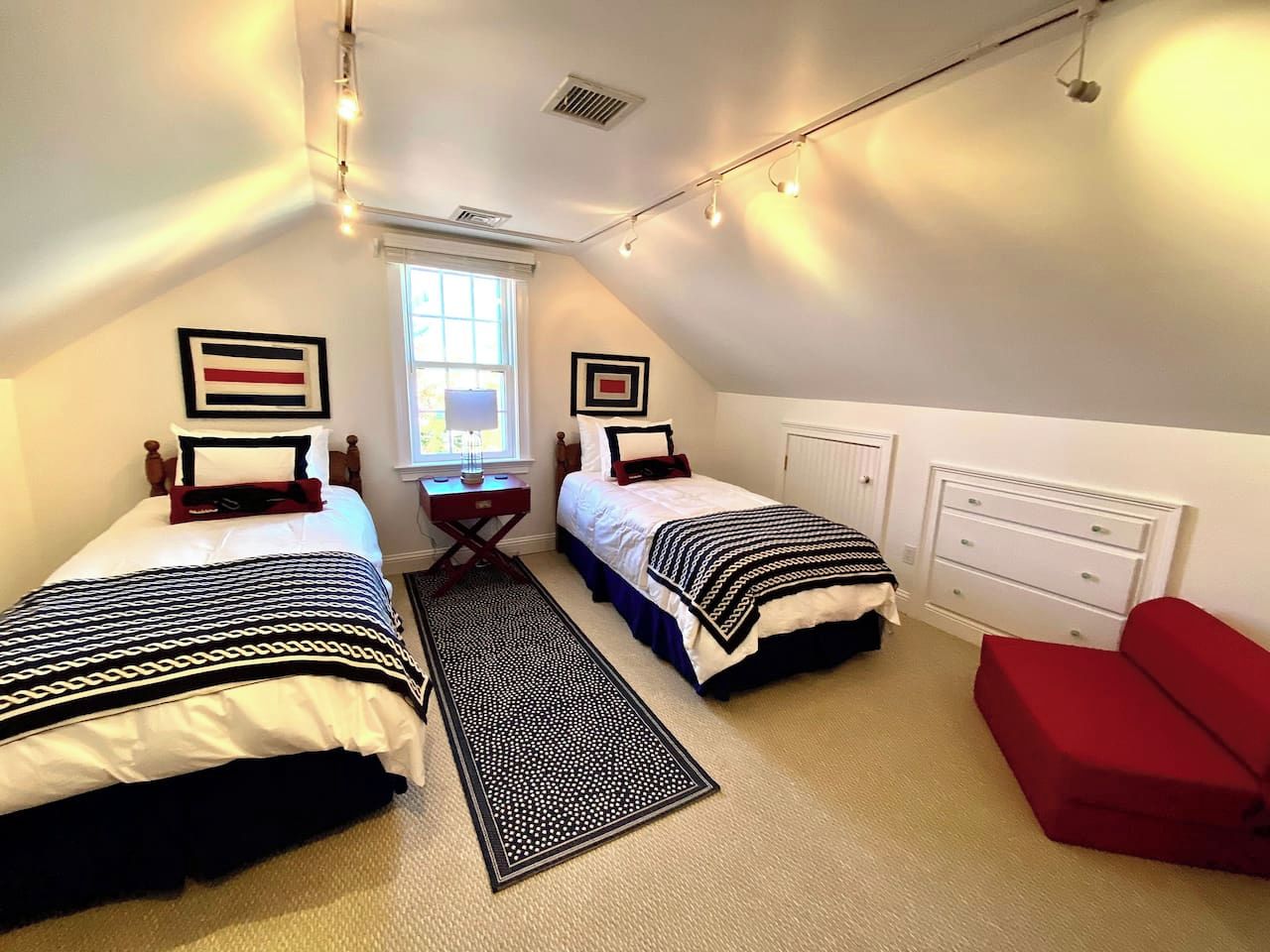 A bedroom with two beds, a red sofa, a small table, and a window.