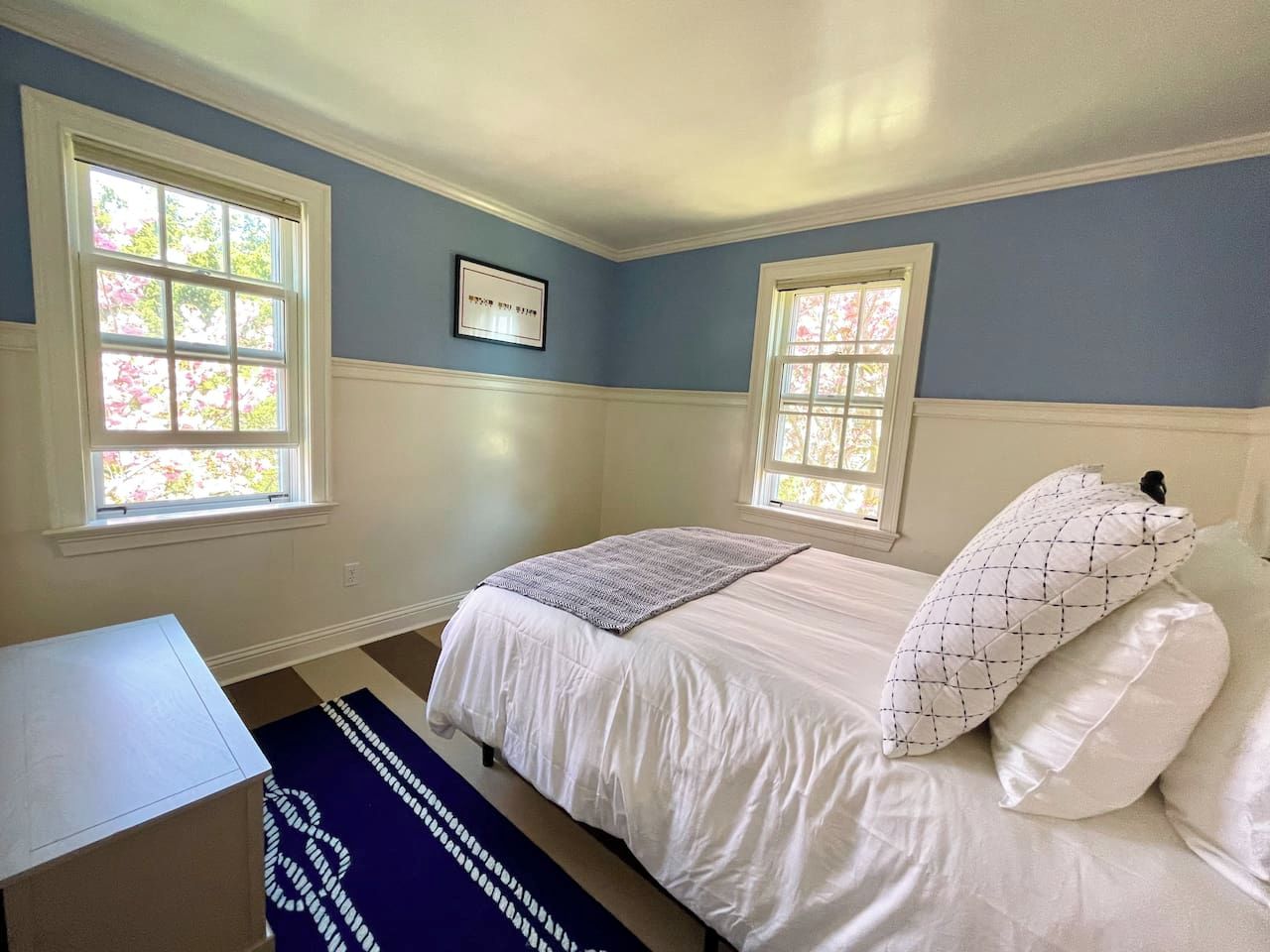 A bedroom with a bed, two windows, a desk, and a rug.