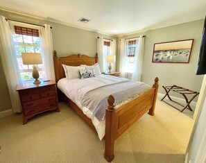 A bedroom with a wooden bed, bedside tables, a lamp, a picture on the wall, and a window with curtains.