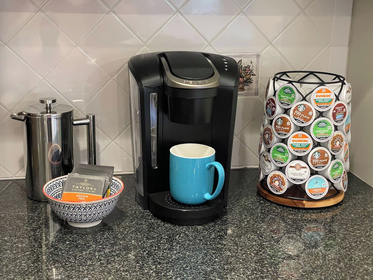 A coffee maker, a blue mug, a basket with tea bags, and a coffee pod holder on a kitchen counter.