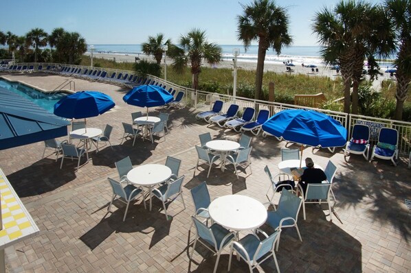 A poolside area with lounge chairs and umbrellas, overlooking a beach.
