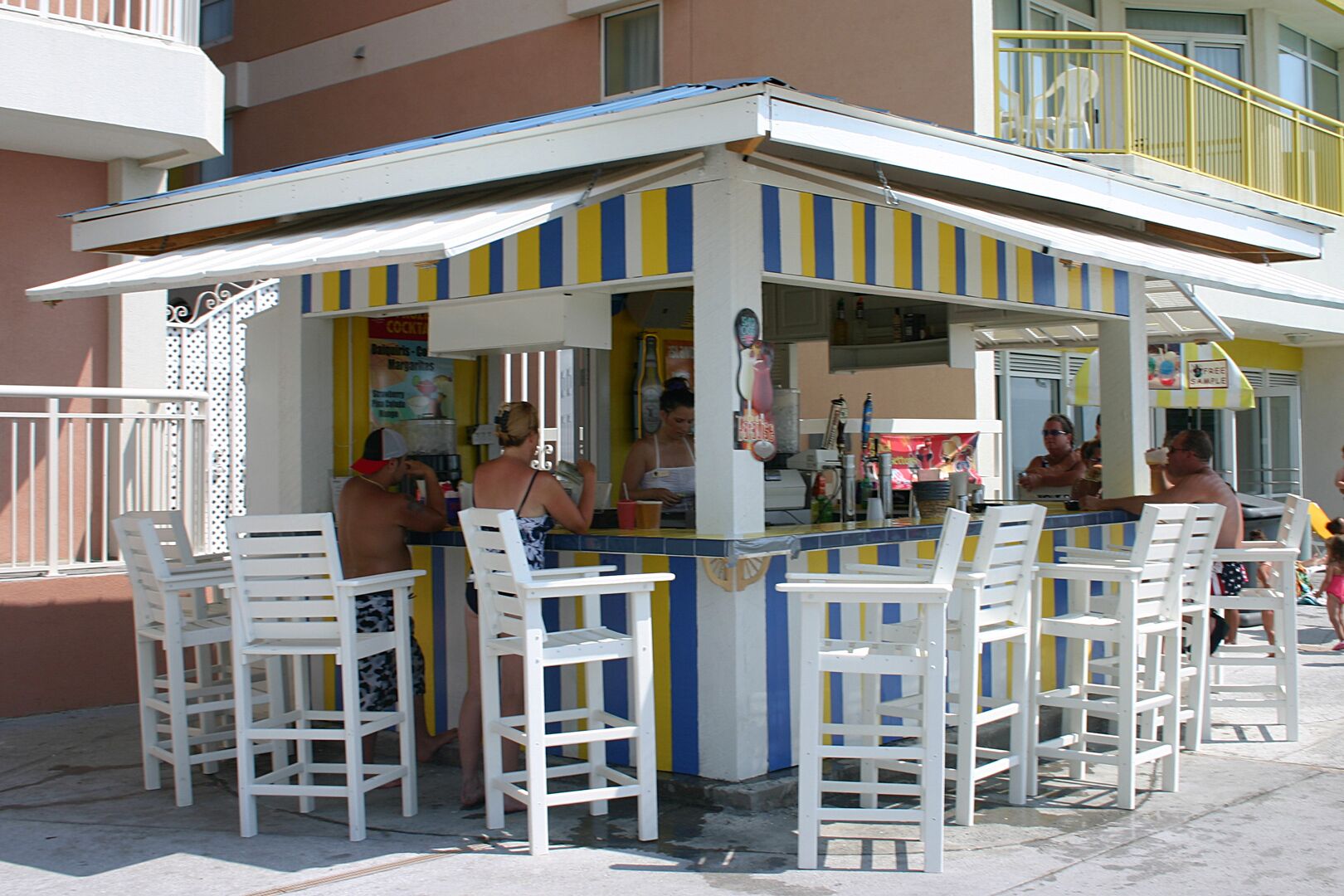 A small outdoor bar with white chairs and a striped awning.