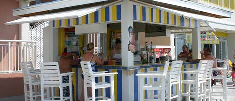 A small outdoor bar with white chairs and a striped awning.