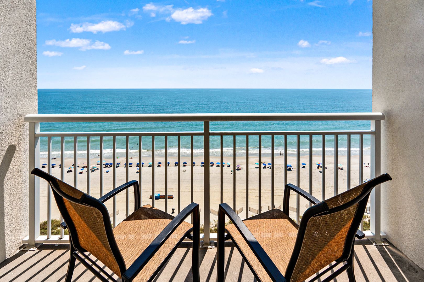 A balcony with two chairs facing a beach.