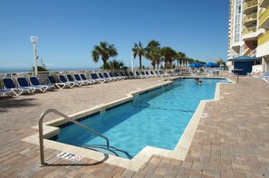 A pool area with blue lounge chairs, a lifeguard sign, and a view of the ocean.