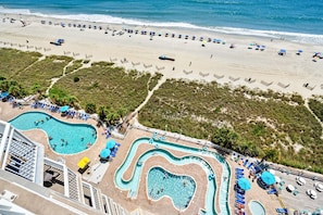A beach resort with multiple swimming pools, sun loungers, and beach umbrellas.