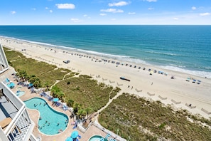 A beach resort with a swimming pool, beach umbrellas, and lounge chairs.