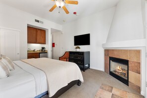 Une chambre à coucher avec un lit, une cheminée, un téléviseur fixé au mur et un ventilateur de plafond.