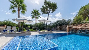 A swimming pool with blue mosaic tiles, surrounded by lounge chairs and umbrellas, with palm trees and a stone wall in the background. - YourHouse Villa Romani con piscina privada y jardín (Muro)
