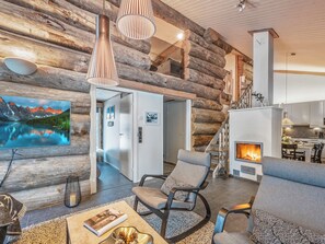 A log cabin interior with a fireplace, seating area, and a painting of a mountain landscape. - Villa rytilampi b by Interhome (Kuusamo)