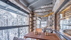 A log cabin interior with a wooden table and chairs, large windows, and a view of a snowy forest. - Villa rytilampi b by Interhome (Kuusamo)
