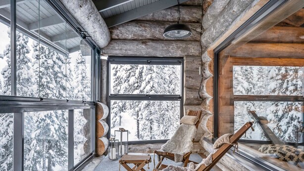 A log cabin interior with large windows, a wooden chair, and a small table. - Villa rytilampi b by Interhome (Kuusamo)