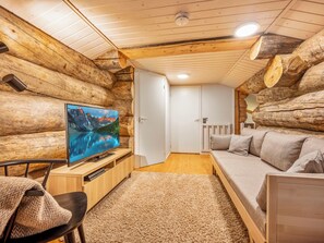 Interior de cabana de tronco com televisão, sofá e piso de madeira.