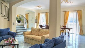 Amplia sala de estar con escaleras, comedor y balcón con cortinas.