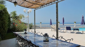 Una terraza exterior con una mesa y sillas de baldosas, sombrillas y vistas al mar.