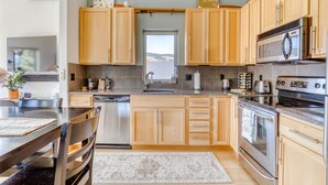 A modern kitchen with wooden cabinets, stainless steel appliances, and a large window. - All About the View - Walk to River, Town, & Trails in Quaint Mosier (Mosier)