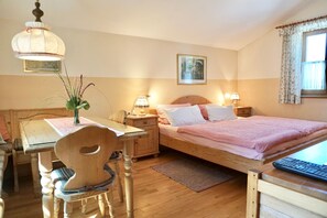 A bedroom with a wooden bed, bedside tables, a desk with a chair, a hanging light fixture, and a window with curtains.