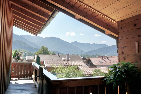 A wooden balcony with a view of mountains and neighboring houses.