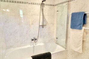 Un baño con ducha envuelta en vidrio, una bañera blanca y un perchero con toallas.