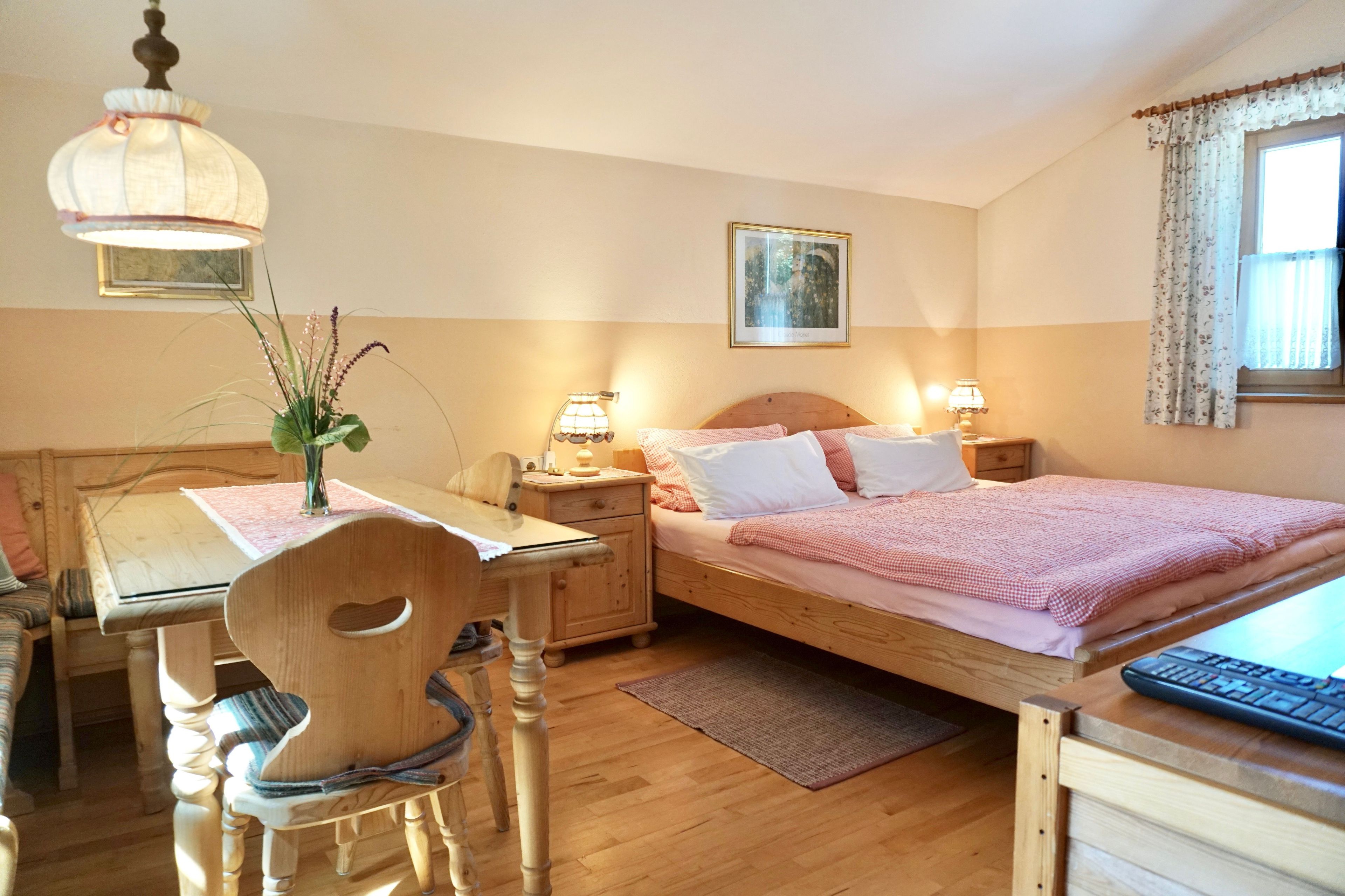 Ein Schlafzimmer mit einem hölzernen Bett, Nachttischen, einem Schreibtisch mit Stuhl, einer Pendelleuchte und einem Fenster mit Vorhängen.
