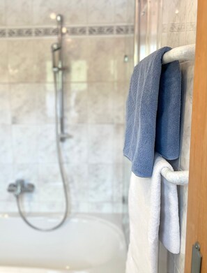 Un baño con cabina de ducha de vidrio, una bañera blanca y toallas colgadas en un perchero.