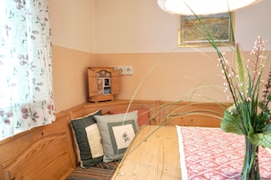 A wooden bench with cushions, a small wooden cabinet, a vase with flowers, and a framed picture on the wall.