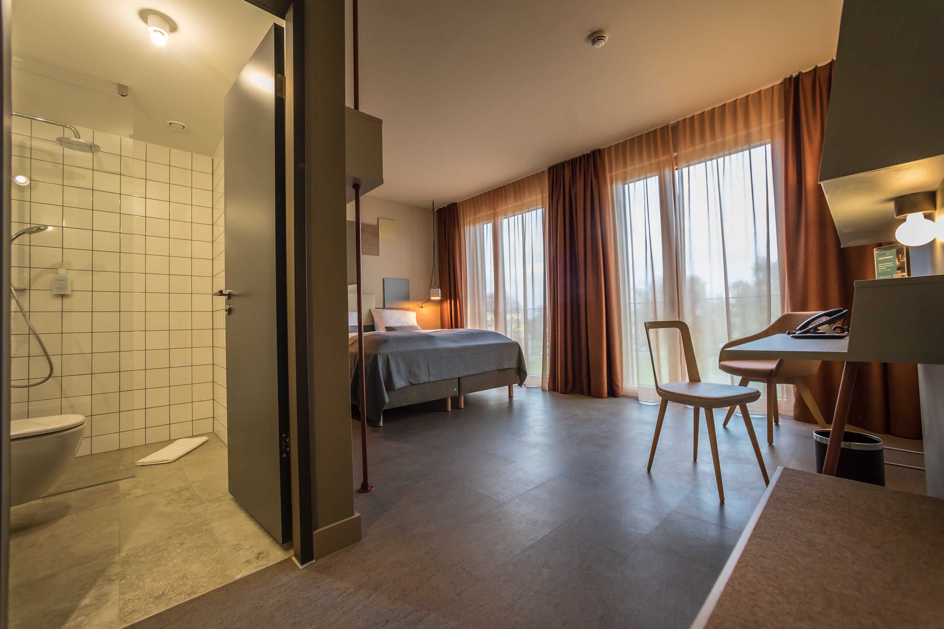 Ein Hotelzimmer mit Dusche, einem Bett, einem Schreibtisch und einem Stuhl.