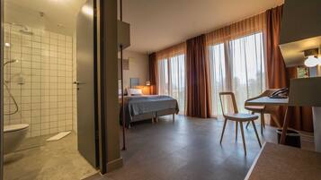 Ein Hotelzimmer mit Dusche, einem Bett, einem Schreibtisch und einem Stuhl.