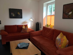 A living room with two red sofas, a wooden coffee table, a floor lamp, and two wall-mounted paintings. - Villa an der Au Phare - Villa an der Au (Fehmarn)