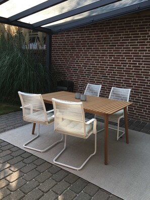 An outdoor patio with a wooden table and white chairs, a brick wall, and a pergola overhead. - Villa an der Au Phare - Villa an der Au (Fehmarn)