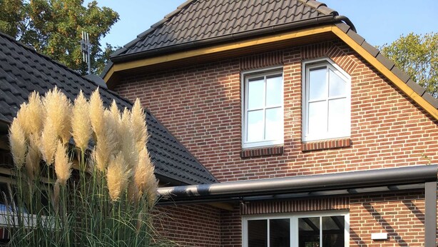 A two-story house with a brick exterior, a covered patio with outdoor furniture, and a well-maintained lawn. - Villa an der Au lighthouse - Villa an der Au (Fehmarn)