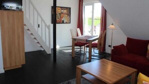 A living room with a wooden coffee table, a red sofa, a dining table with chairs, and a staircase. - Villa an der Au lighthouse - Villa an der Au (Fehmarn)