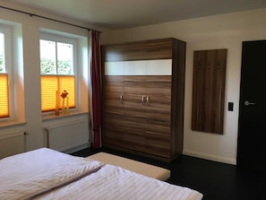 A bedroom with a bed, a wardrobe, a radiator, and a window with blinds. - Villa an der Au Phare - Villa an der Au (Fehmarn)
