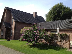 A brick house with a tiled roof, a garden with flowering bushes, and a white statue. - Villa an der Au Phare - Villa an der Au (Fehmarn)