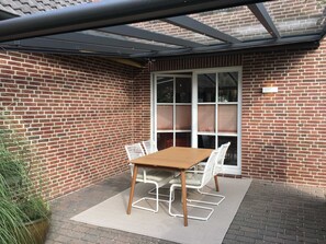 Een terras met een tafel, stoelen, een glazen deur en een bakstenen muur.