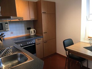 Een compacte keuken met een Bosch magnetron, een waterkoker, een spoelbak en houten kastjes.