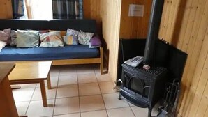 Una habitación con suelo de madera, un sofá con cojines, una mesita y un estufa de leña.