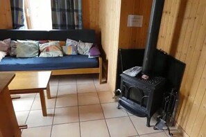 Ein Zimmer mit Holzboden, einer Couch mit Kissen, einem kleinen Tisch und einem Kaminofen.