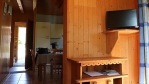 Un interior de madera con un televisor montado en la pared, una pequeña mesa con papeles y una cocina al fondo.