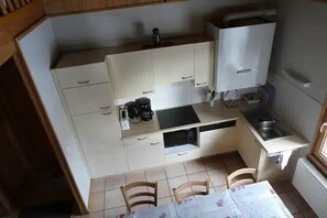 Eine kleine Küche mit Esstisch, Stühlen, einer Kaffeemaschine und einem Kühlschrank.