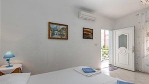 Habitación de hotel con cama, dos cuadros, aire acondicionado, puerta y ventana con vista a un balcón.