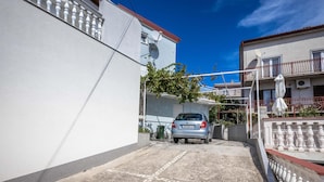 Una calle estrecha con un coche estacionado, edificios blancos con balcones y un cielo azul despejado.