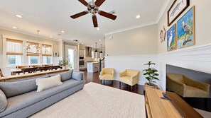 A spacious living room with a sofa, chairs, a fireplace, and a dining area with tables and chairs. - The Den on 30A - 3BR/2.5BA Prominence Home - Sleeps 8 - Golf Cart & Ping Pong Table (Santa Rosa Beach)