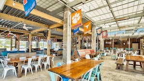 An indoor dining area with multiple wooden tables and chairs, some with blue cushions.