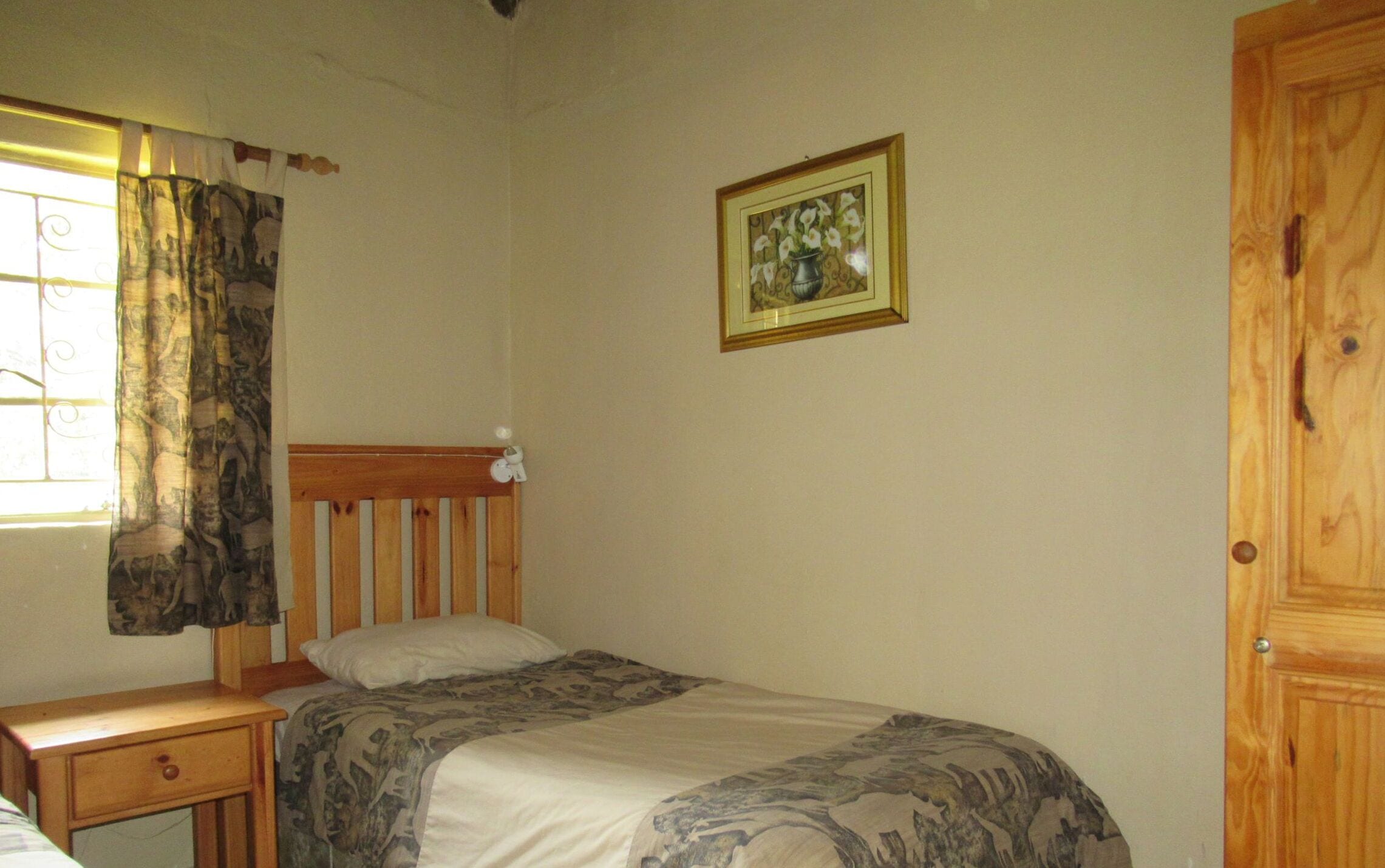 Een slaapkamer met een enkel bed, een nachtkastje, een raam met gordijnen en een deur.