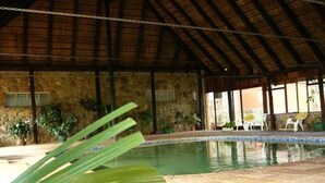 Un área de piscina con pared de piedra, techo de paja y plantas en macetas.