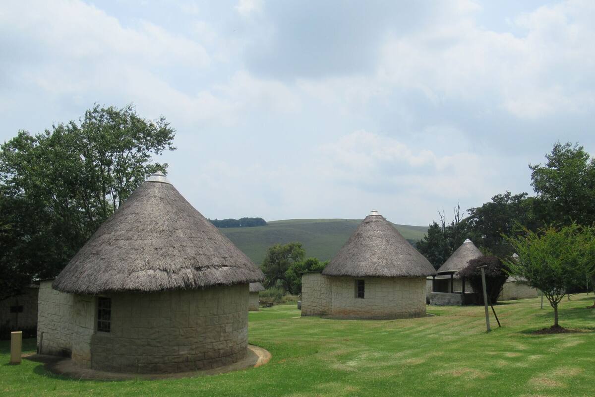 A rural setting with thatched-roof cottages surrounded by greenery and hills in the background.