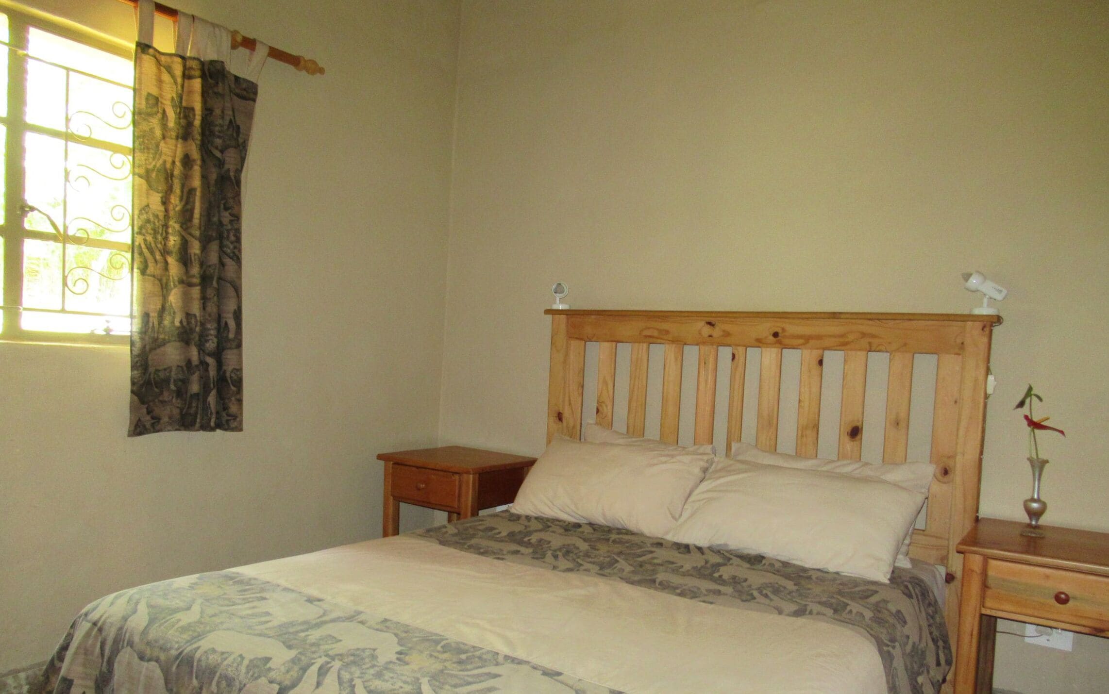 Un dormitorio con una cama de madera, una mesita de noche, una lámpara y una ventana con cortinas.